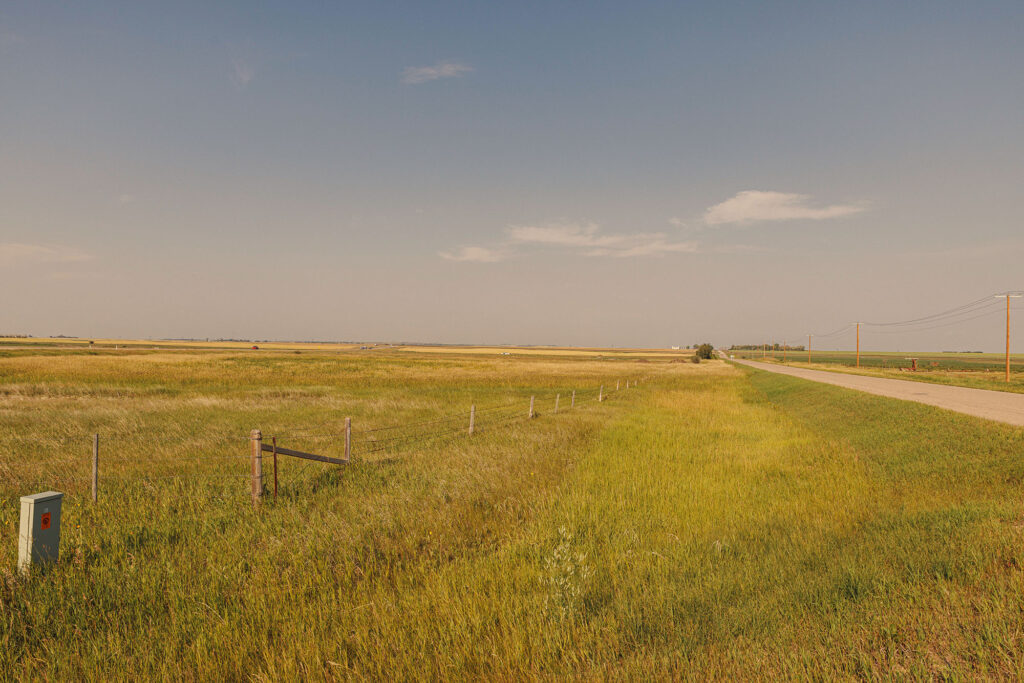 McKay Lands Parcel 10 - A stretch of highway and telephone poles along a large green and gold fenced in field