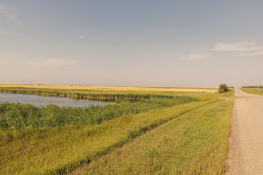 McKay Lands Parcel 5 - A long stretch of highway runs next to farm land with a body of water in the middle of the farm land