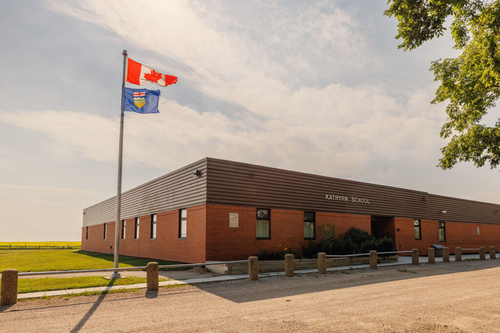 McKay Lands community - The Canadian flag and Alberta flag on a pole blowing in the wind above the Kathyrn School